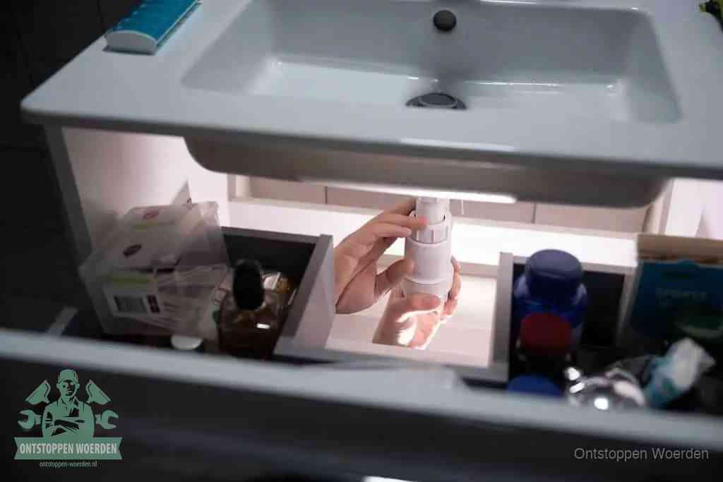 Een pompfles met zeep boven een wastafel, de heet water en afwasmiddel-methode om een vetprop in de afvoer los te maken in Woerden