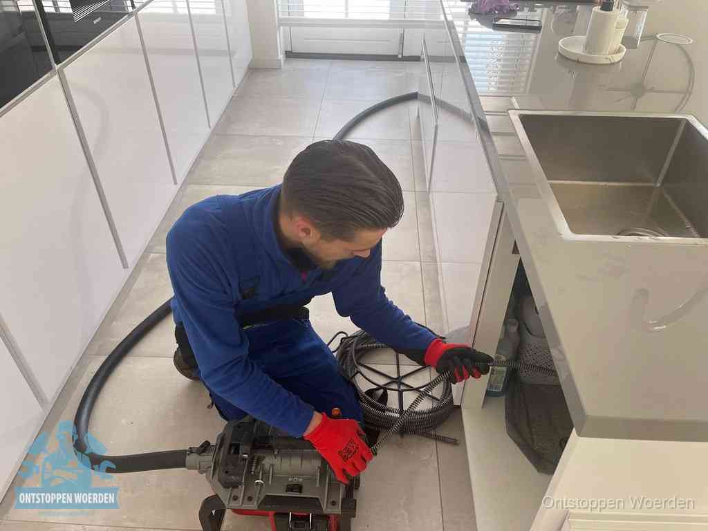 Een monteur ontstopt de keukenafvoer onder de spoelbak met een elektrische veermachine in Woerden
