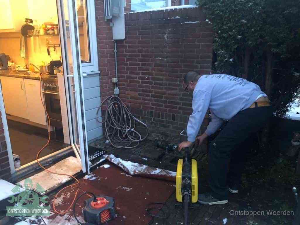 Een monteur werkt buiten bij een open riool-/grondput met een elektrische ontstoppingsmachine om een verborgen afvoerprobleem op te sporen in Woerden