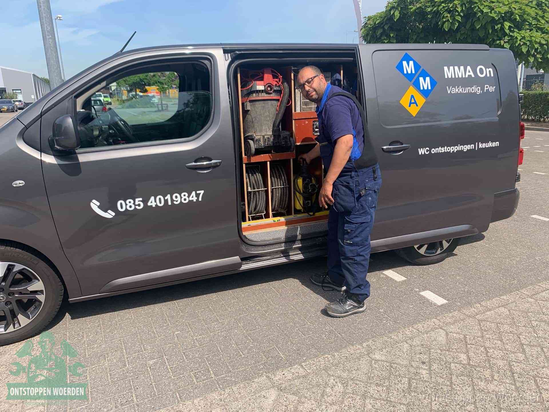 Een monteur bij de open schuifdeur van zijn bedrijfsbus op een parkeerplaats, klaar om de oorzaak van terugkerende afvoerverstoppingen aan te pakken in Woerden