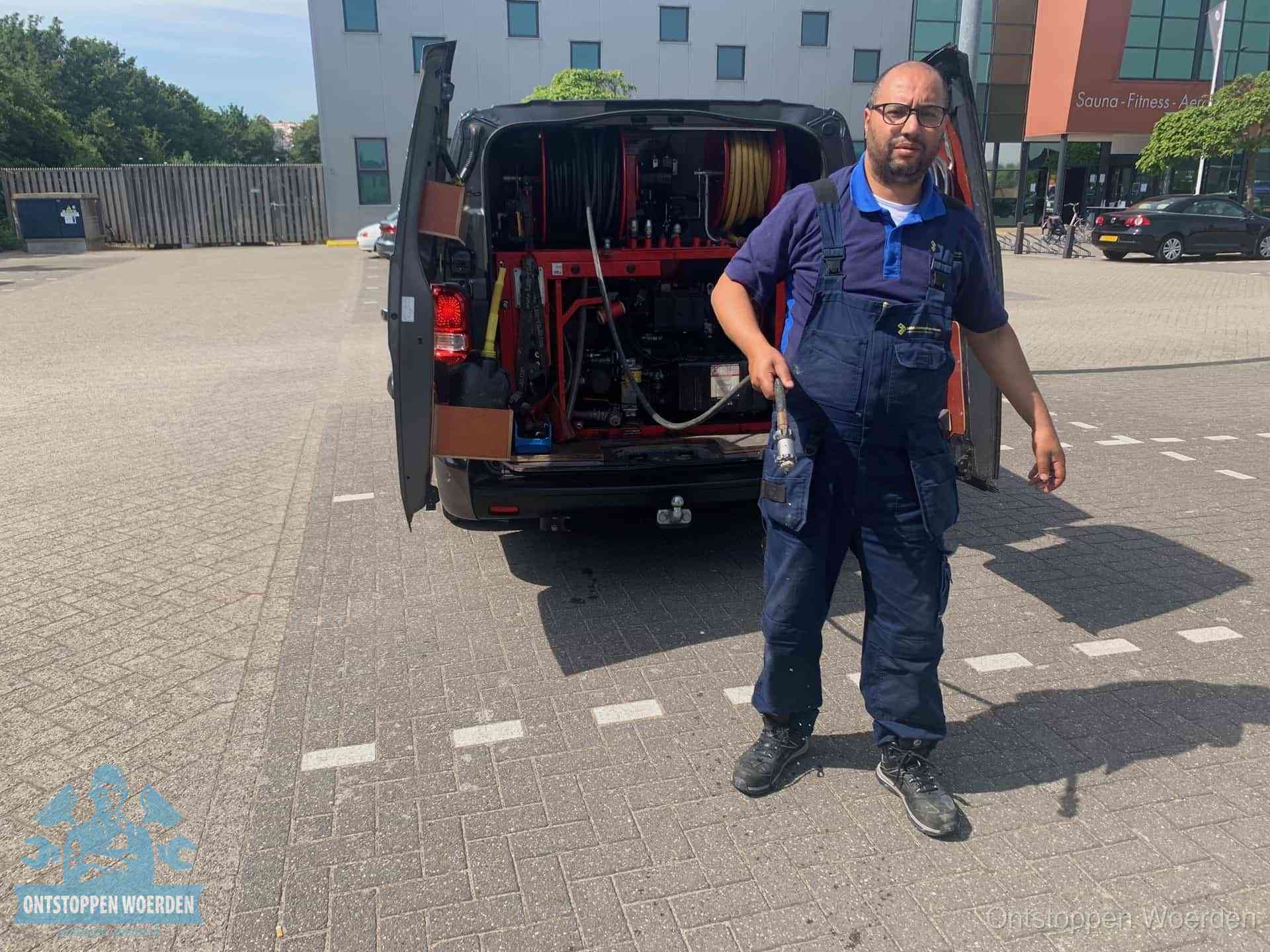 Een monteur bij zijn bestelbus met een hogedruk- en rioolreinigingsunit, klaar om de oorzaak van terugkerende wc-verstoppingen aan te pakken in Woerden