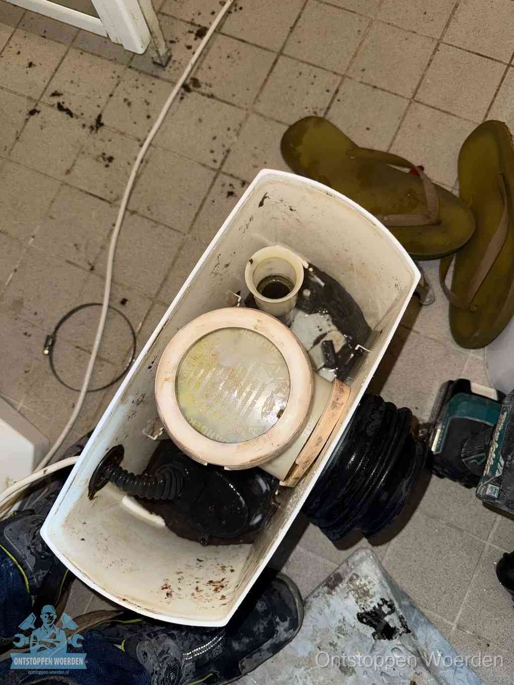 Een gedemonteerde toiletpot op de vloer met ontstoppingsveer en gereedschap ernaast, het verwijderen van een vastzittend voorwerp uit de wc in Woerden