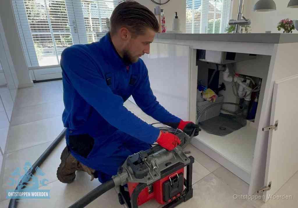 Een monteur voert een professionele elektrische ontstoppingsmachine in de afvoer onder de spoelbak tijdens het gootsteen ontstoppen in Woerden